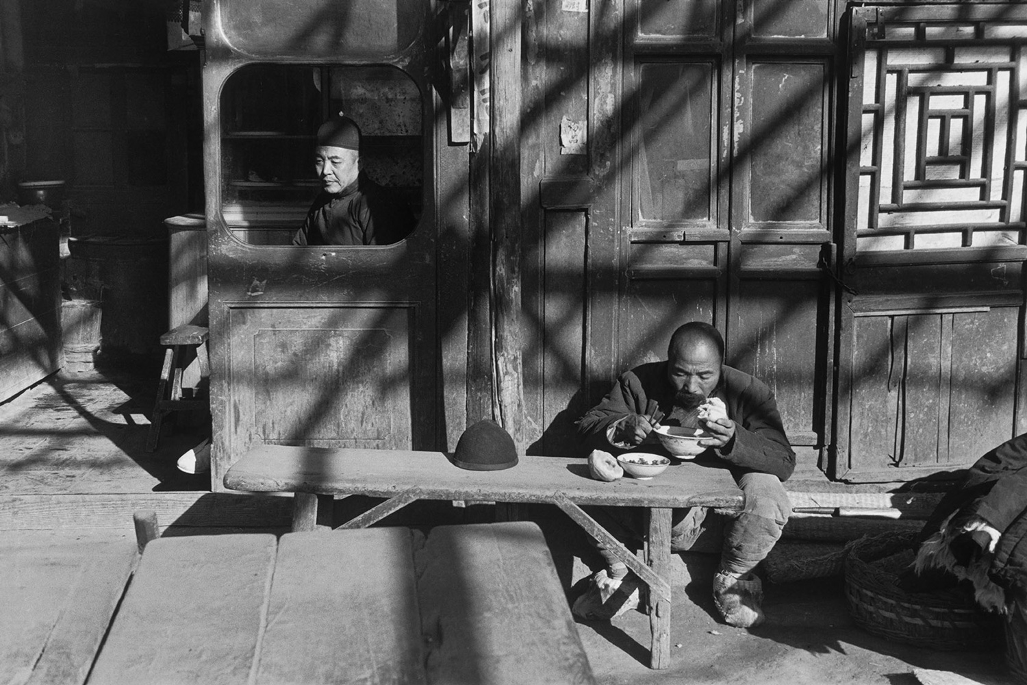 Pechino, dicembre 1948 Un cameriere o un negoziante siede alla finestra aperta di un'osteria, mentre un cliente mangia fuori sotto un pergolato.